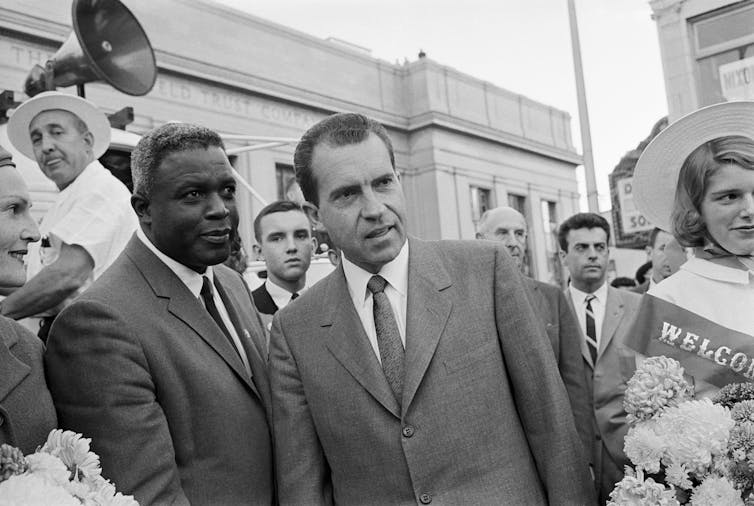 A Black and white man are seen standing next to each other in a crowd of people.