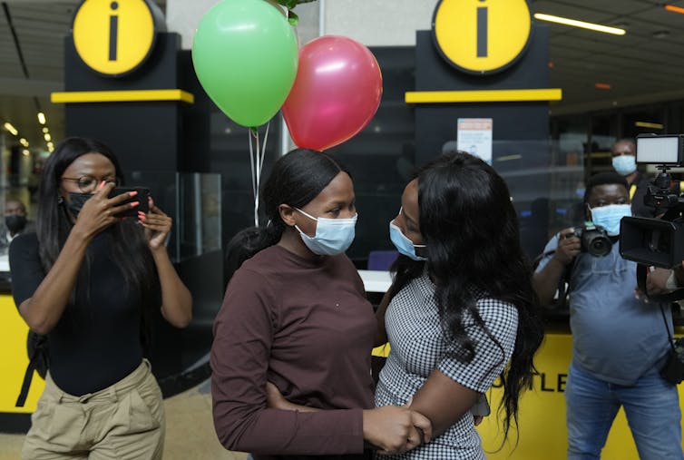 Deux jeunes femmes se tiennent par la main, dans un aéroport