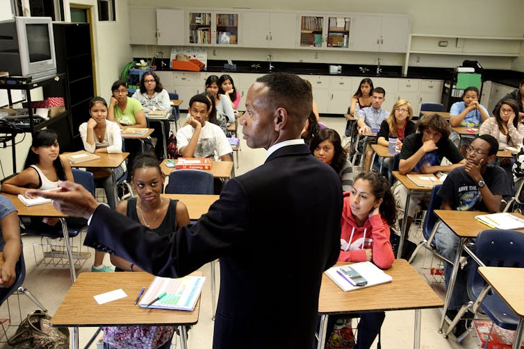 A Black man teaches a classroom full of students.