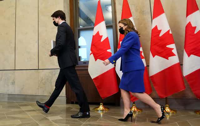 A man and a woman in business attire walk past a row of Canadian flags