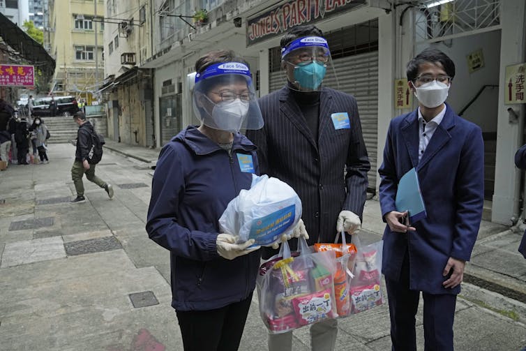 Three people in face masks and shields carrying bags and packages.