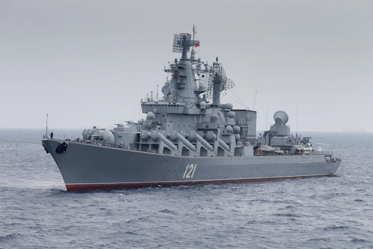 a large gray naval ship with big guns sails through choppy waters