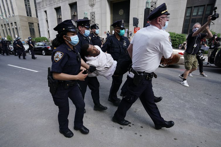 Des policiers new-yorkais portent des masques et portent un jeune homme noir par tous ses membres dans une rue.