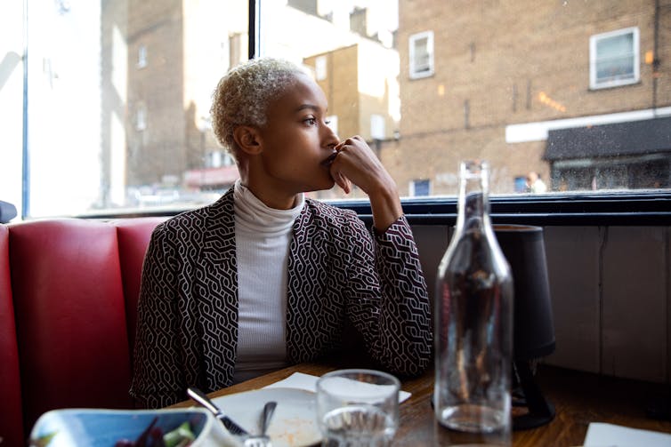 woman seated in restaurant booth looks out the window pensively