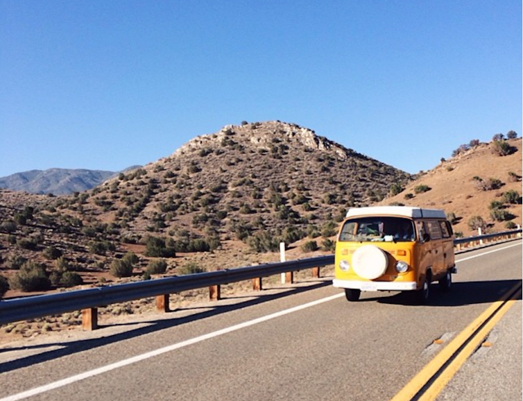 Yellow van driving on the open road with mountains in the background