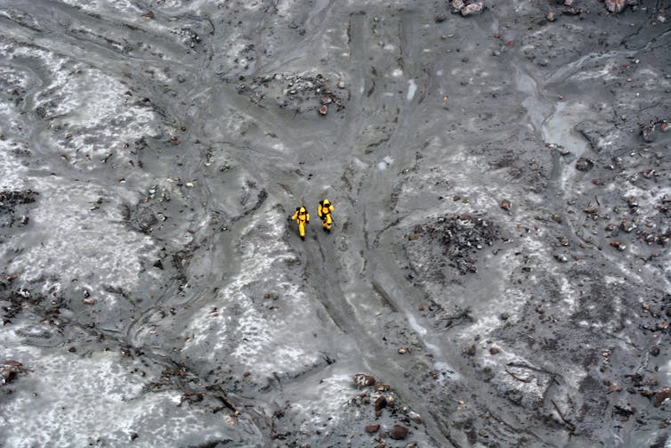 Two rescuers seen walking across an ash field on Whakaari White Island in December 2019.