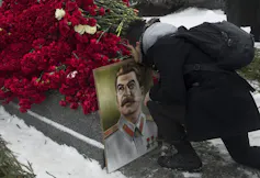 A man kisses a portrait of Stalin by a grave covered with red roses.