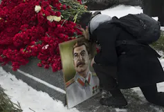A man kisses a portrait of Stalin by a grave covered with red roses.