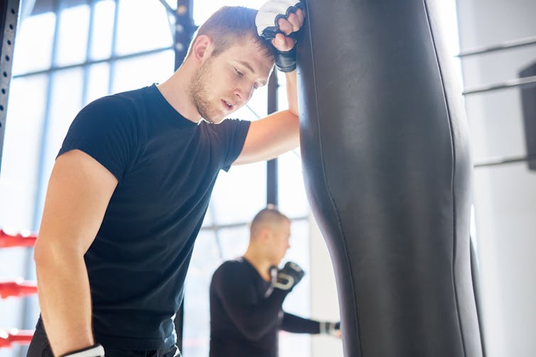 Man leaning on boxing bag to take a rest