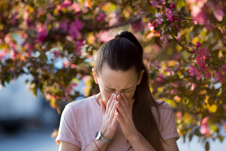 Mujer estornudando frente a árbol en flor.