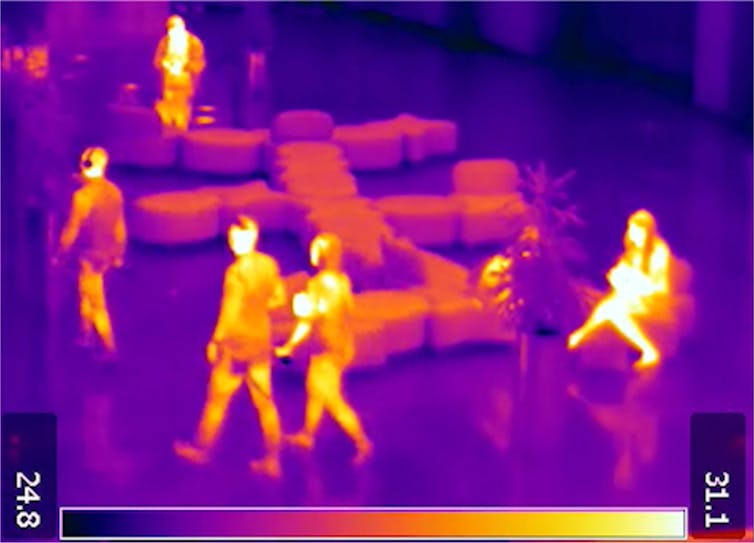 An infrared-colour image of people walking and sitting in a room