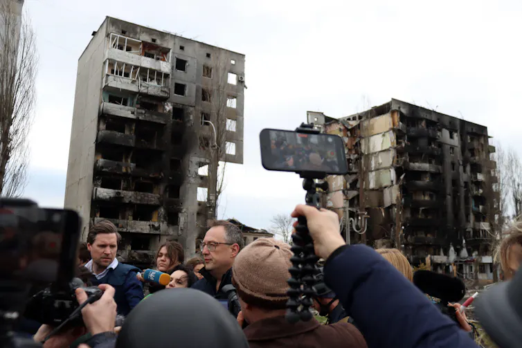 A reporter holds up a mobile phone to film a Ukrainian government press briefing in the town of Borodyanka, north of Kyiv, April 2022.