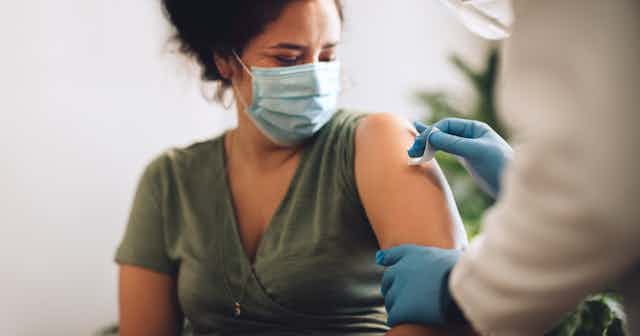 A woman has her upper arm prepared to receive the COVID-19 vaccine.