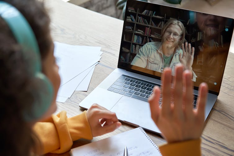 a teacher on a laptop screen waves at a student