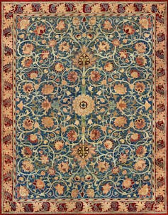 A carpet with an orange, burgundy and rust floral design over a teal background with a circular centre.