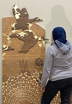 A pattern etched goose is examined by a viewer wearing a hijab, seen from behind.