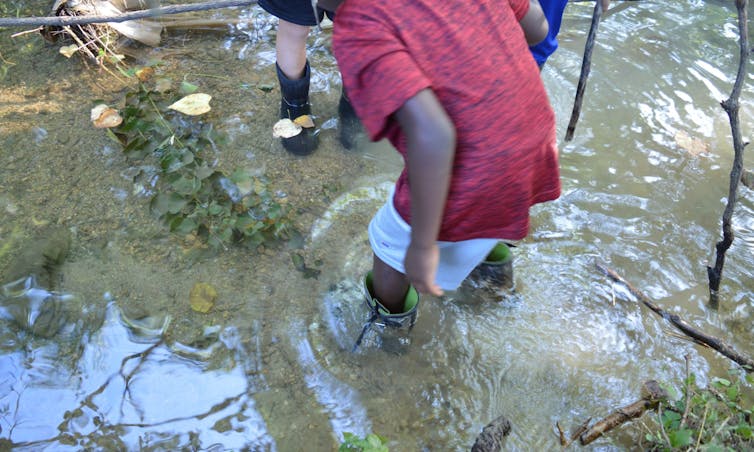 Children's feet in boots are seen wading in water.