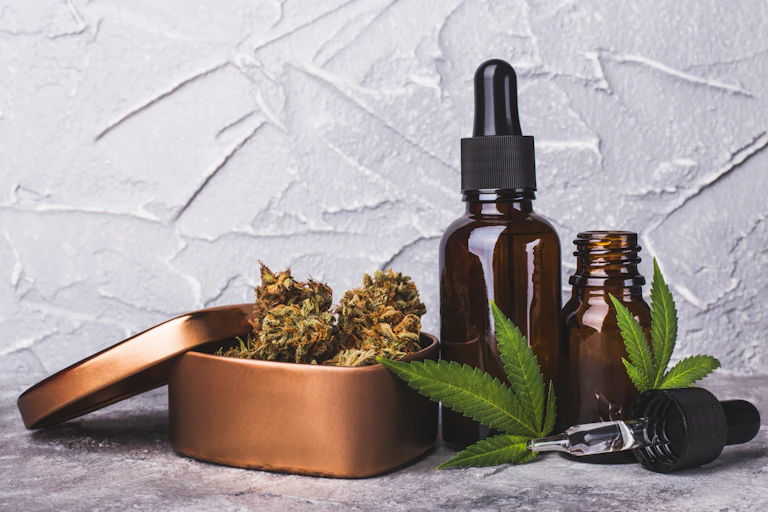 Two small, brown glass bottles with droppers, two marijuana leaves and a copper-colored box of dried marijuana