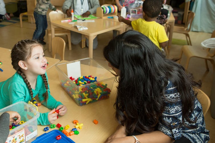 A child seen in conversation with an educator at a table.