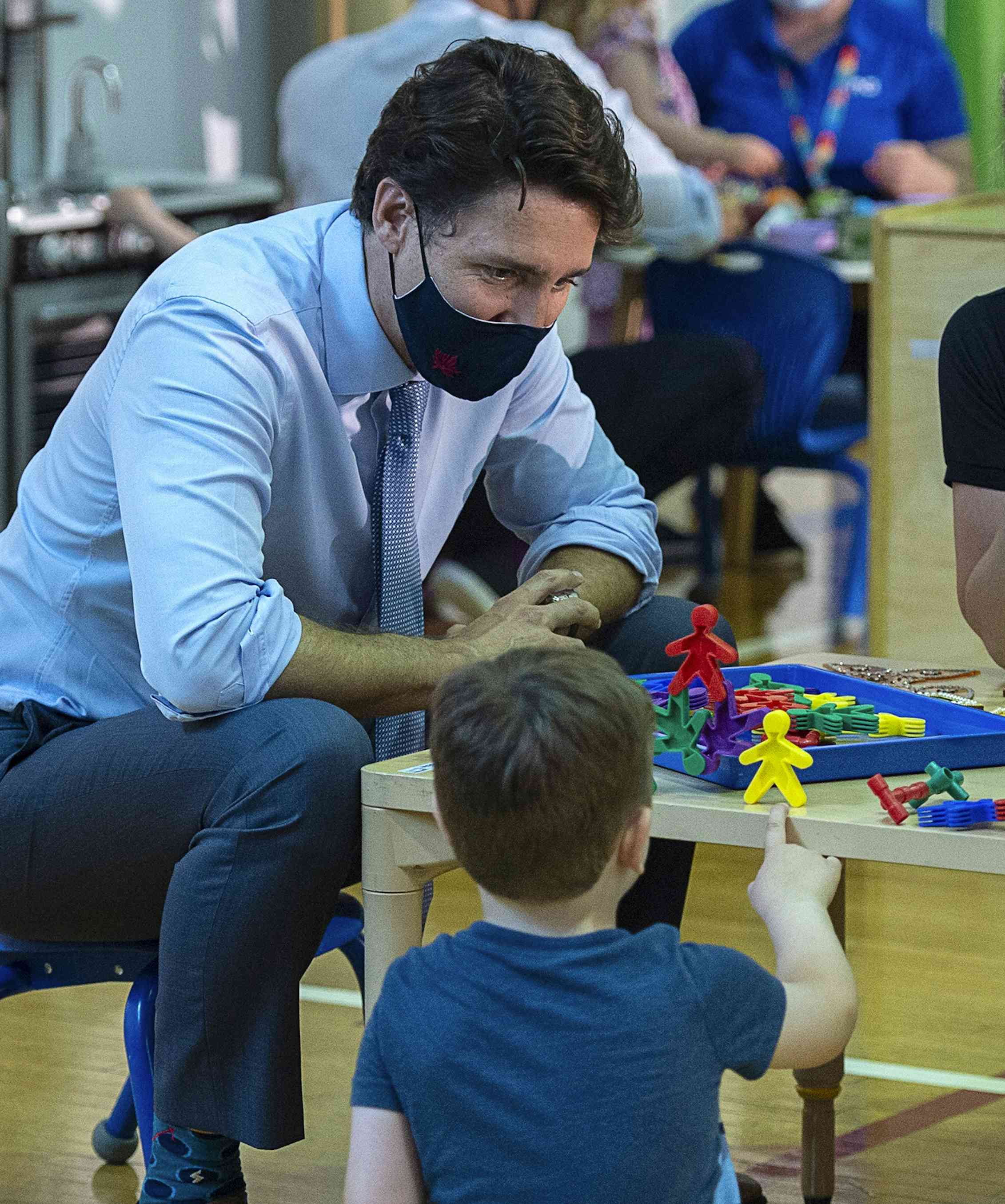 Prime Minister Trudeau seen in a tie and face mask crouching at a child care centre.