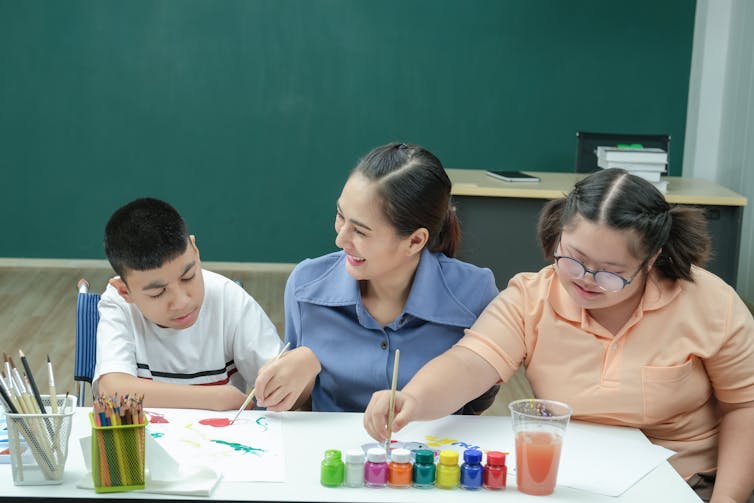 Woman helping two disabled children in a classroom