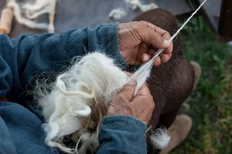 A pair of elderly hands spin a clump of wool into yarn.