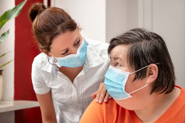 Intellectually disabled woman in a mask smiles at her carer.