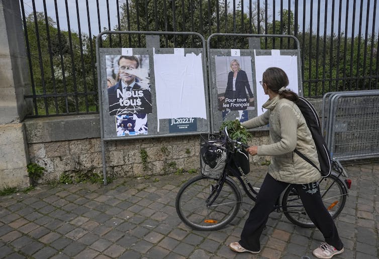 A woman pushes her bike past campaign posters ahead of the final vote.