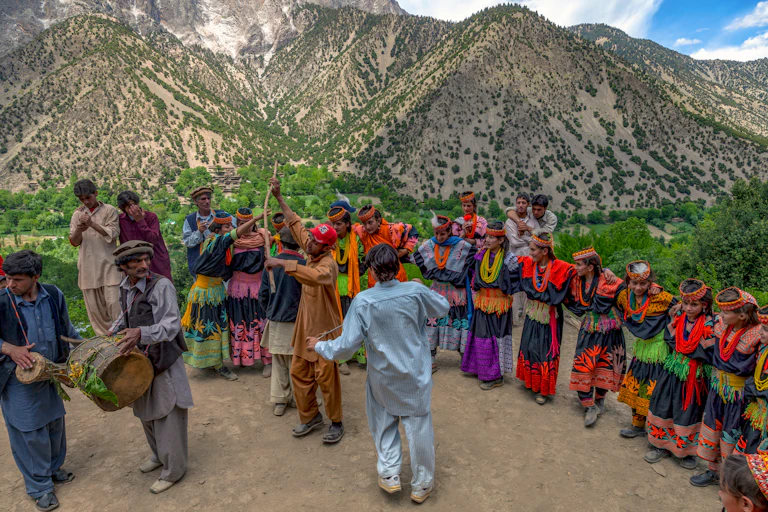 Men with musical instruments with dancers in colourful clothes behind and mountains in the background.