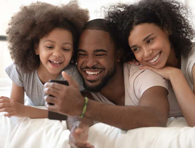 A smiling couple and child with the man taking a selfie of the family