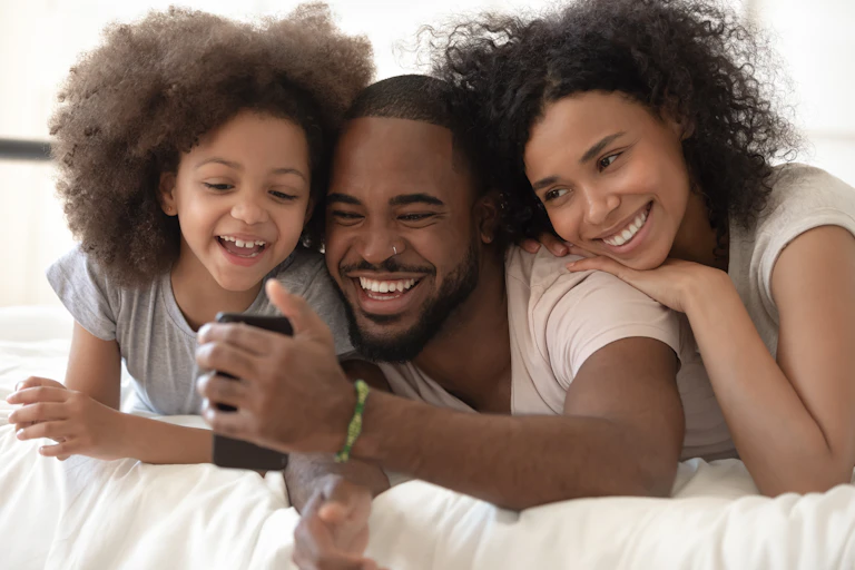 A smiling couple and child with the man taking a selfie of the family