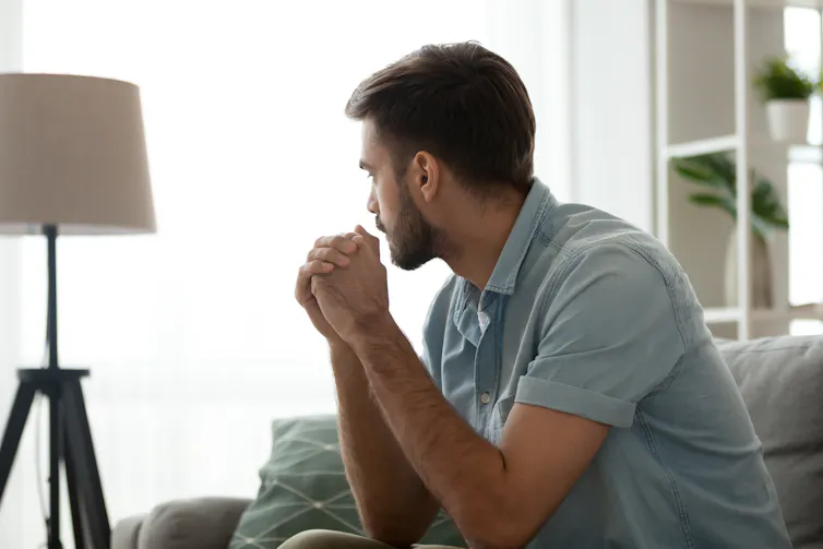 A man with a beard sitting alone looking away from the camera toward a window