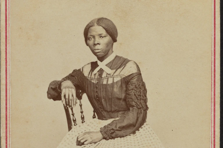 A black woman dressed in a black and white gown is sitting on a chair.