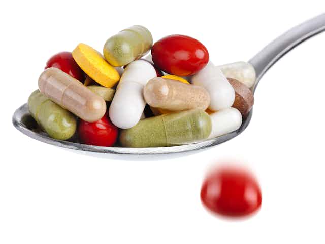 Spoon piled high with mixed colors and shapes of pills, against a white background.