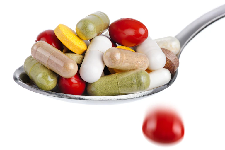 Spoon piled high with mixed colors and shapes of pills, against a white background.