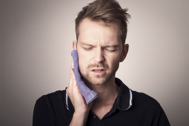 A man holding a compress to his jaw and wincing