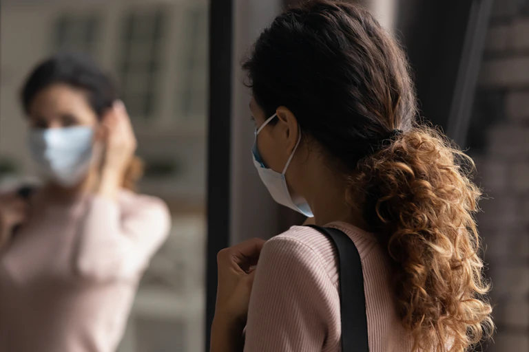 Woman putting on mask looking in mirror about to leave house