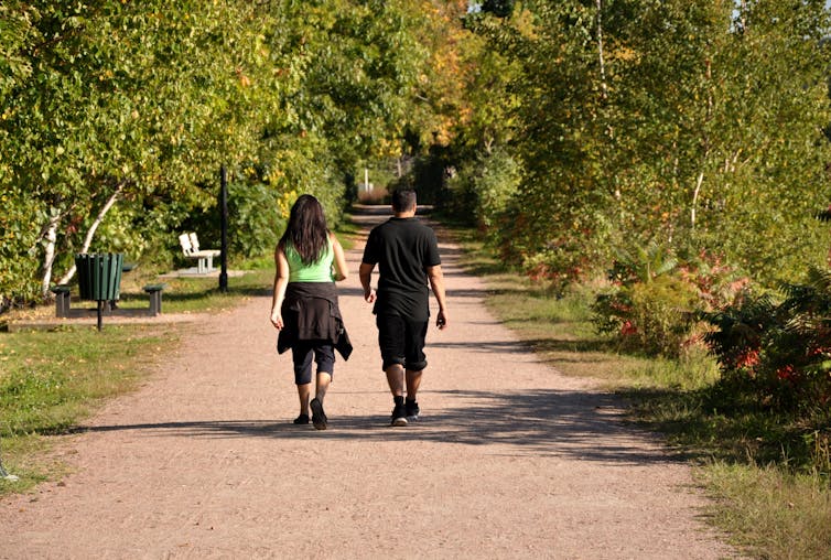 Young adult man and woman go for a brisk walk in the park on a sunny day.