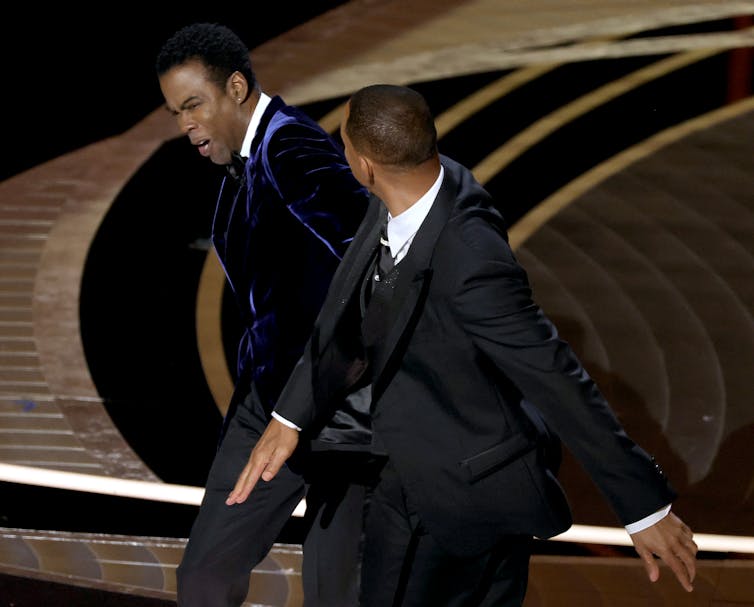 A well-dressed Black man slaps another well-dressed Black man.