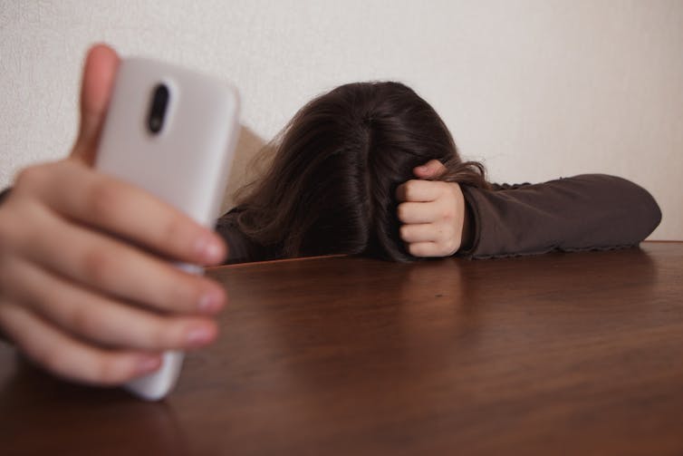 a woman holding a mobile phone has her forehead on a table