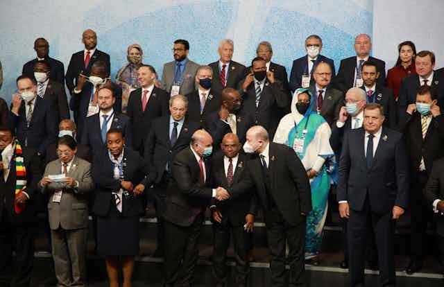 Leaders of non-aligned states pose for a photo, some shaking hands, most wearing masks.