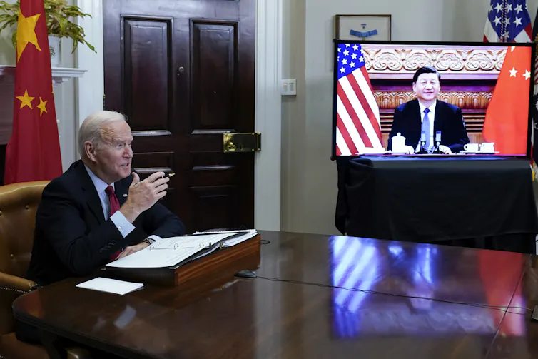 Joe Biden, assis, et Xi Jinping, sur un écran de télévision