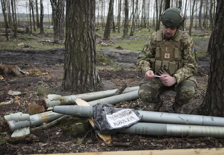 Un soldat est assis à côté de missiles, dans une forêt
