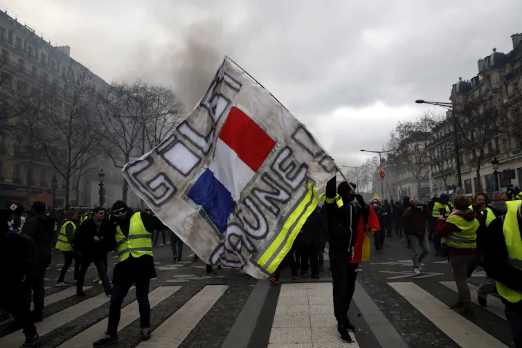 Des manifestants portant un gilet jaune tiennent une banderole