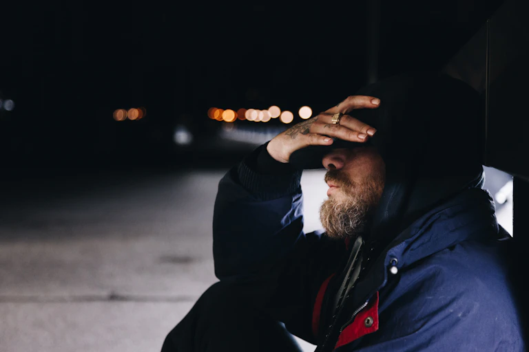Man sits with street background, covering face