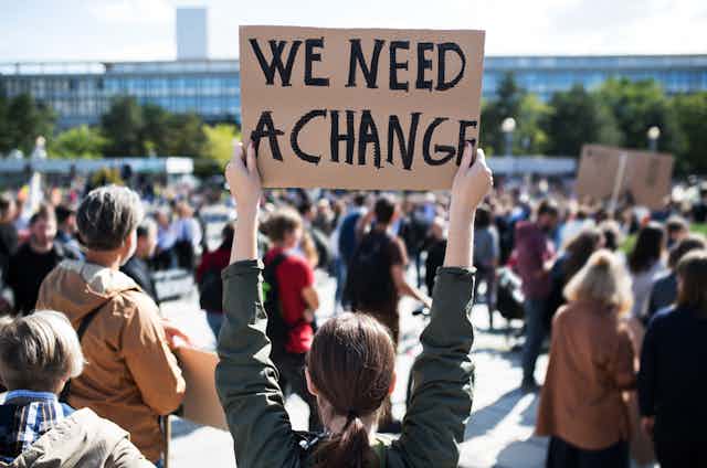 Mujer en manifestación con una pancarta en la que pone "we need a change"