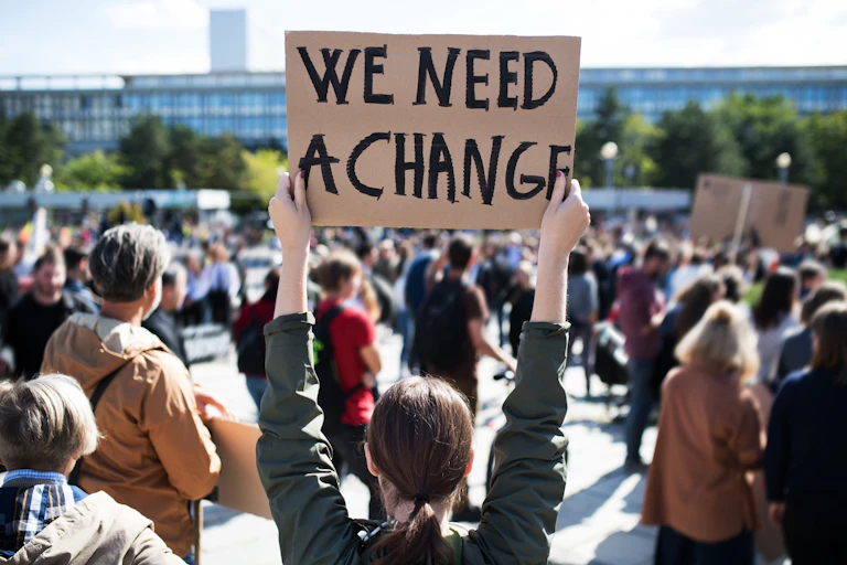 Mujer en manifestación con una pancarta en la que pone "we need a change"