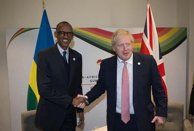 Boris Johnson and Paul Kagame, president of Rwanda, shake hands in front of their countries' flags.