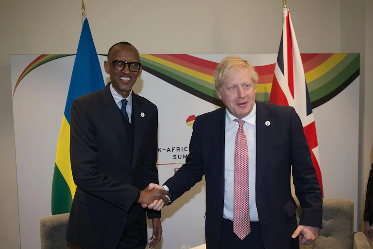 Boris Johnson and Paul Kagame, president of Rwanda, shake hands in front of their countries' flags.
