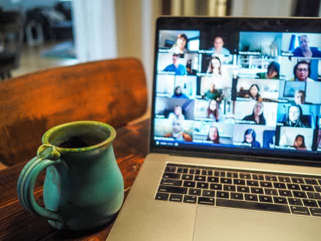 A coffee mug sits next to a laptop, the screen is displaying a zoom call with blurred faces.